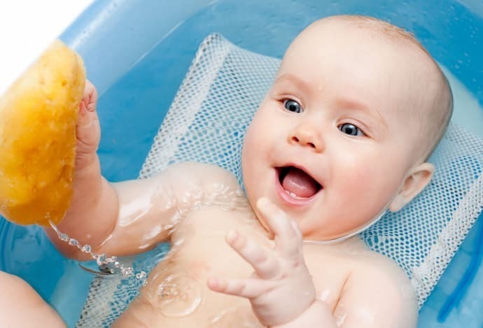 Bebê em banheira azul com almofada para banho branca.