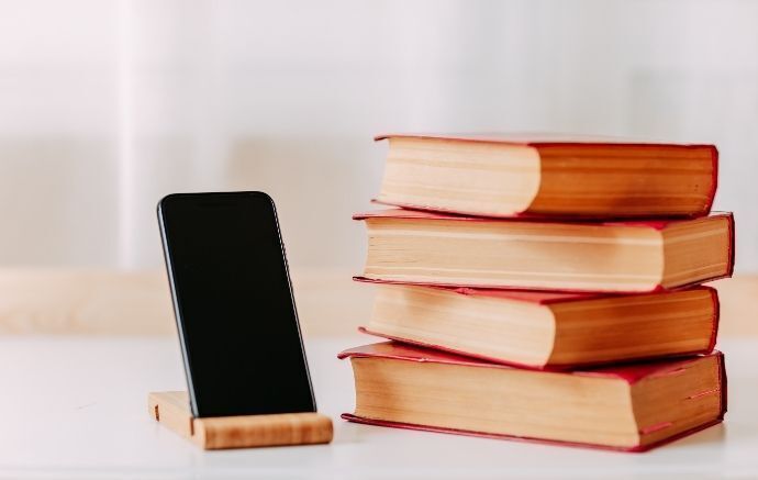 Celular em suporte de mesa de madeira ao lado de livros.