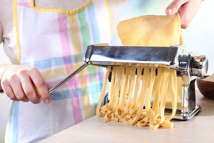 Mulher fazendo macarrão em máquina manual.