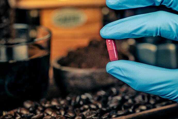 Cafeína em capsula sendo segurado por alguém de luva