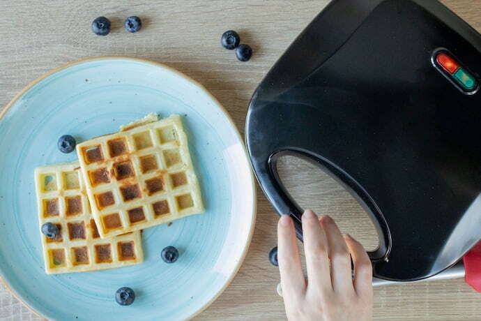 máquina de waffle ao lado de um prato com dois waffle