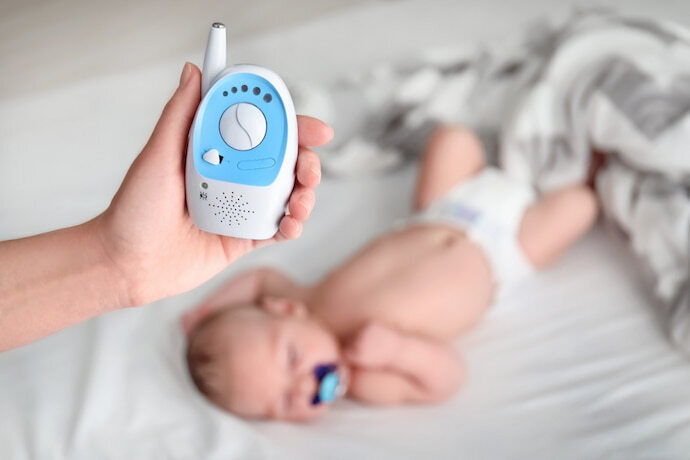 alguém segurando uma babá eletrônica e ao fundo bebe dormindo