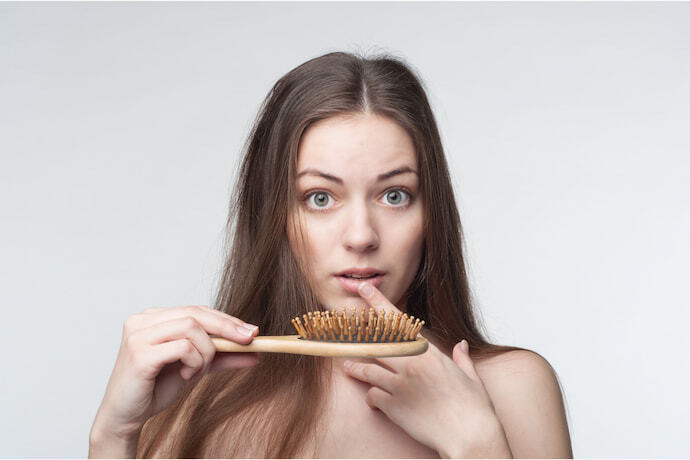 Mulher com escova e assustada com queda de cabelo.