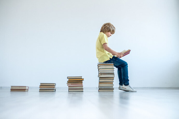 Menino sentado em pilha de livros.