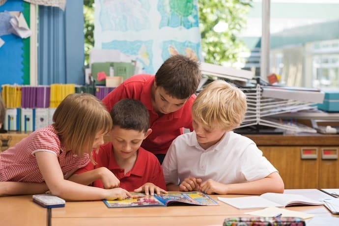 Crianças na escola lendo gibi juntos.