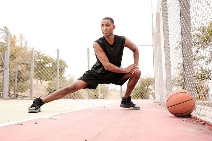 Homem se alongando com tênis e bola de basquete.