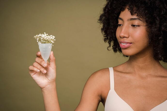 Mulher sorrindo segurando coletor menstrual transparente com flores dentro.