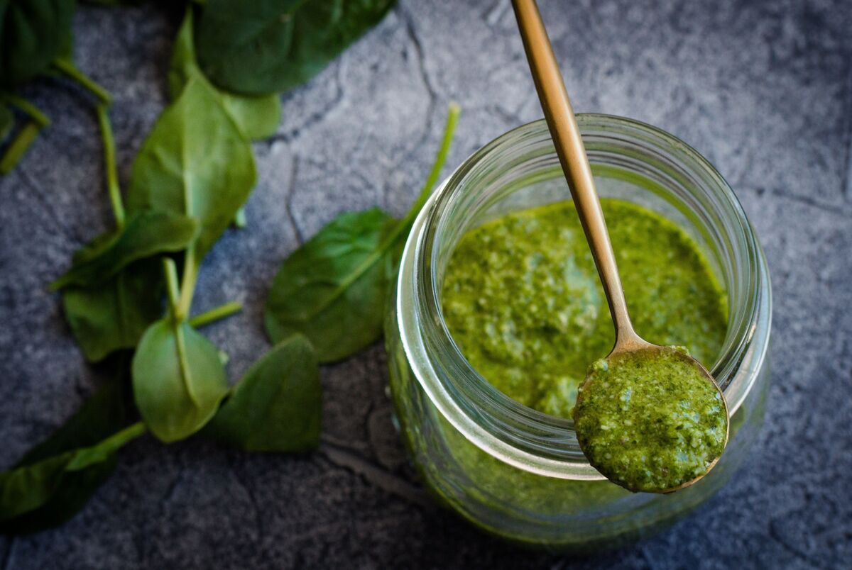 Molho pesto em recipiente de vidro e folhas em volta