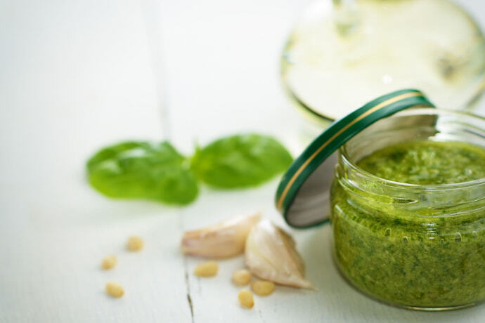 Molho pesto em recipiente de vidro e ingredientes em volta