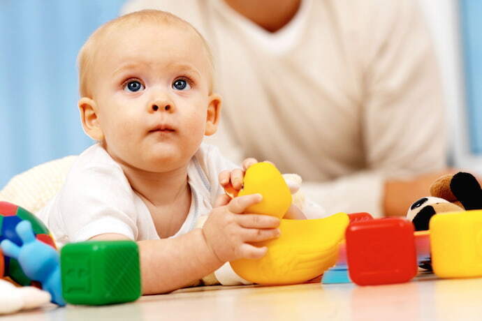 Bebê segurando patinho de brinquedo com brinquedos em volta.