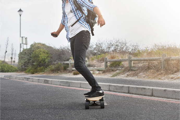 Homem andando em skate elétrico segurando controle remoto.