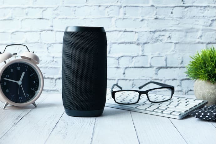 Smart speaker preta em mesa com itens de escritório.