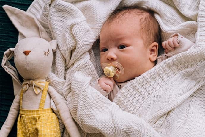 Bebê deitado com coberto e chupeta.