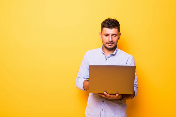 Homem segurando notebook em fundo amarelo.