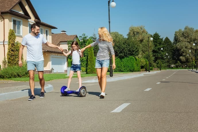 Pais segurando filha andando em hoverboard.