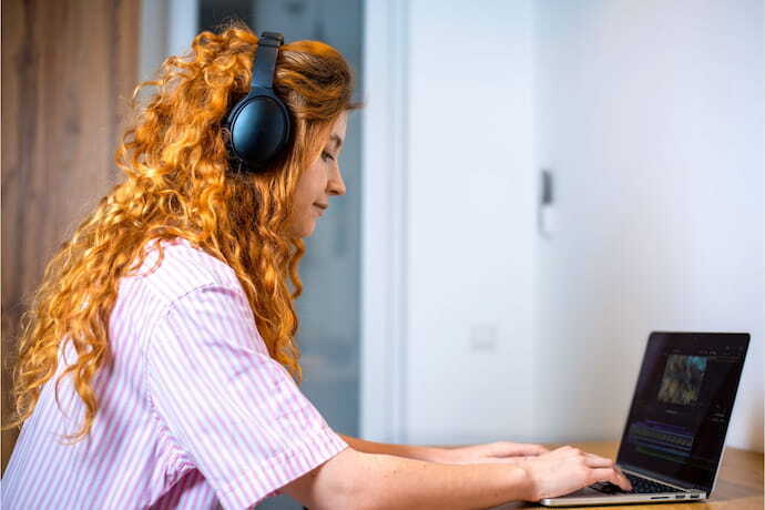 Mulher editando vídeo em notebook com fone de ouvido.