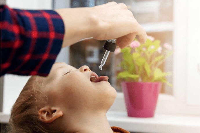 Pessoa dando vitamina B para menino em gotas.