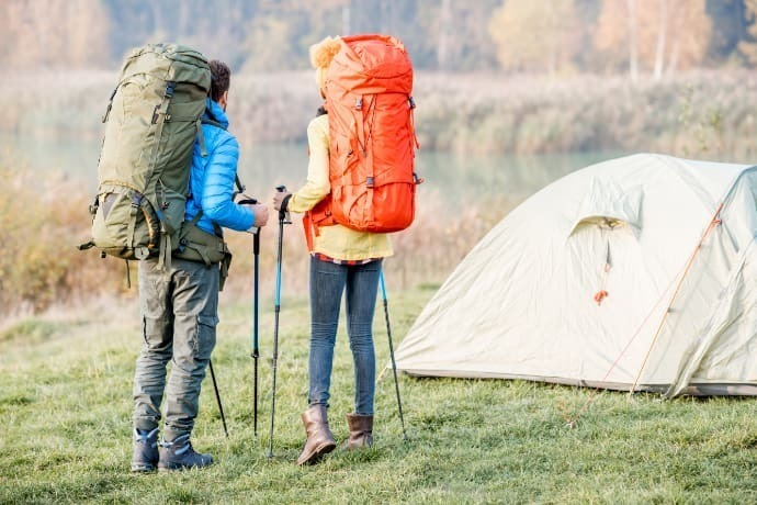 Casal na floresta com mochilas nas costas e uma barraca