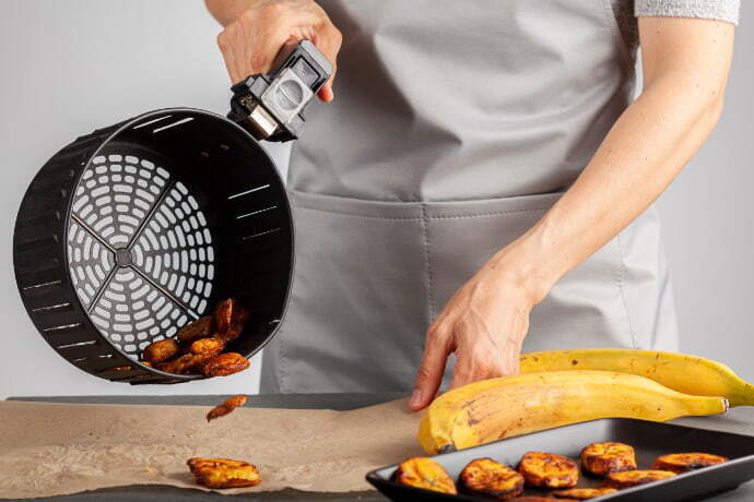 Indivíduo despejando na mesa da cozinha fatias de banana da terra assada.