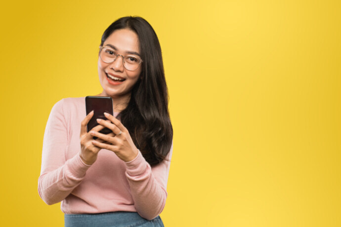 Mulher mexendo no celular em um fundo amarelo