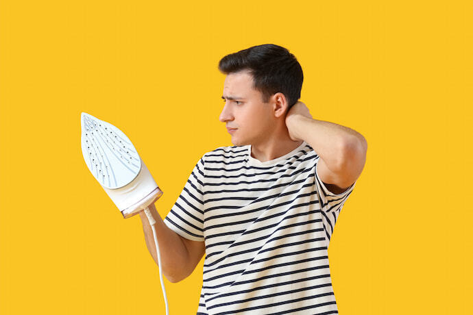 Homem segurando um ferro de passar roupa em um fundo amarelo.