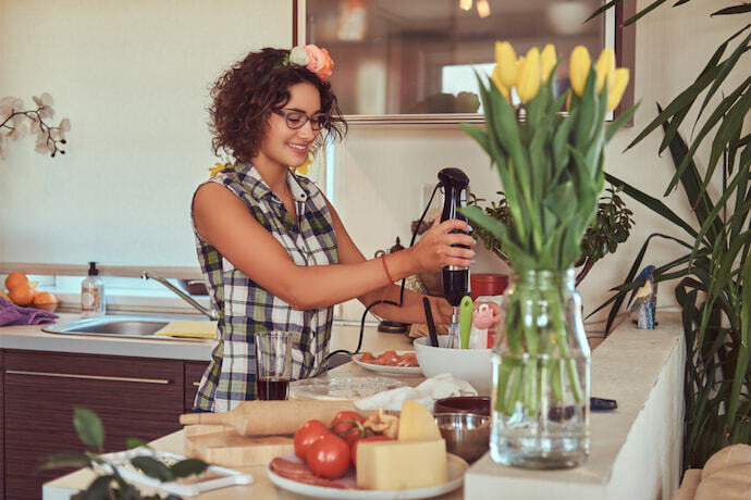 Mulher preparando o alimento com o auxílio de mixer de mão na cozinha.