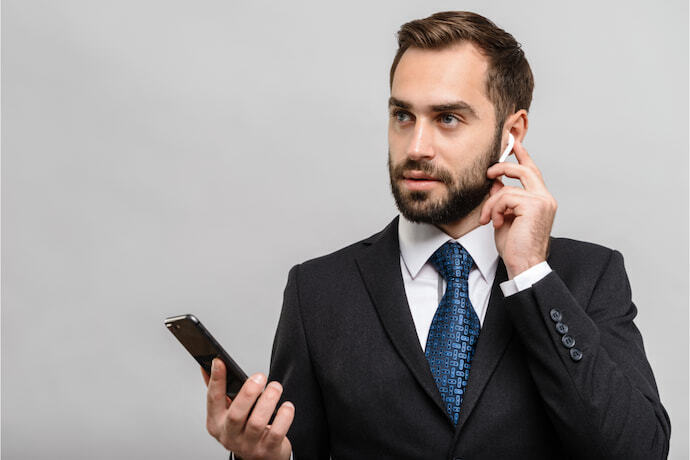 Homem de terno com fones sem fio em um fundo cinza.