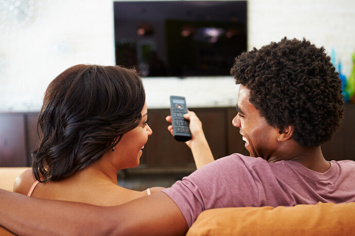 Casal na sala de estar, sentados no sofá e assistindo TV.