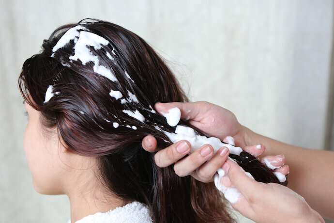 Mãos aplicando creme hidratante no cabelo da mulher.