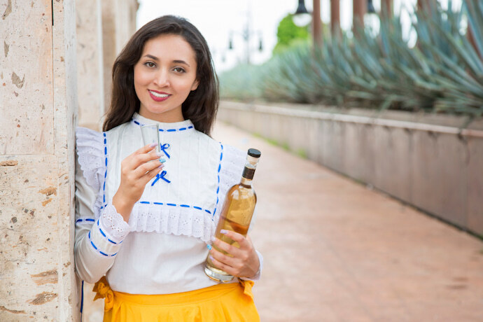 Mulher ao ar livre, segurando uma garrafa de tequila e um copo.