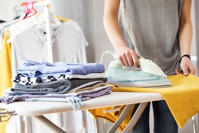 Roupas sobre tábua de passar e pessoa passando roupa ao lado