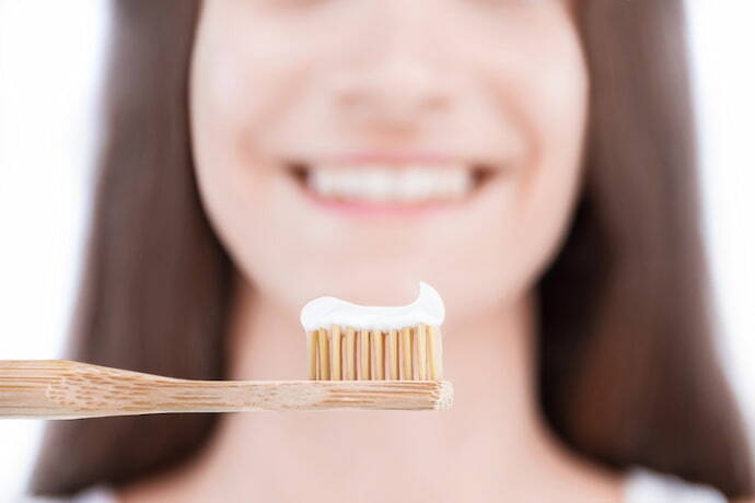 Pasta de dente na escova e ao fundo uma mulher desfocada