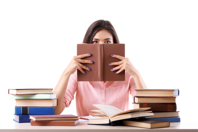 Mulher segurando um livro e vários livros sobre a mesa