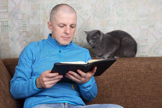 Homem lendo um livro no sofá e próximo de um gato