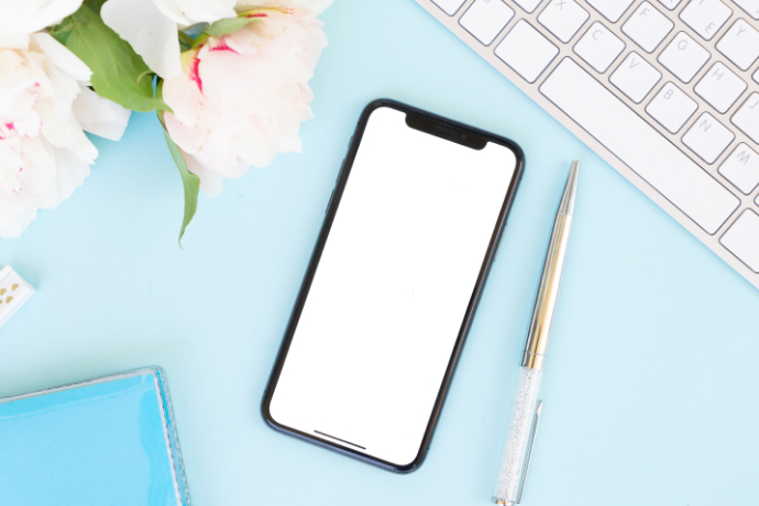 Celular, caneta, teclado e flores sobre a mesa