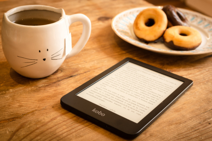 E-book, xícara de chá e um prato com donuts sobre a mesa