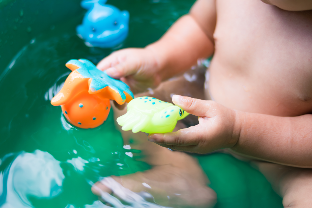 bebê na banheira com brinquedos na mão